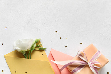 Envelopes, gift box and flowers on light background