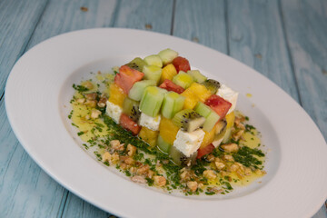Recipe for sweet and sour salad, feta cheese, cucumber, tomato, kiwi, mango, oil and lemon sauce, parsley and nuts. High quality photo
