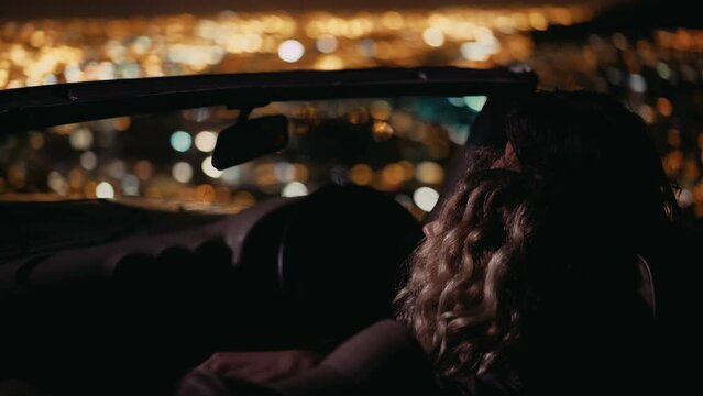 Young couple looking at night city lights in a convertible