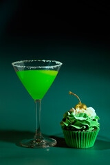 Lucky Green St. Patrick's Day Green Martini Cocktail  and a Chocolate Cupcake Topped with Green Icing and a Gold Cherry on a Green Background