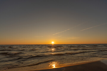 Fototapeta premium Sunset in a cloudless sky on the coast of the Gulf of Finland in Ust-Narva. The sky is clear, the waves gently roll on the sand. Estonia, Narva-Jyesuu. Natural background. Space for text.