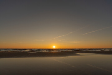 Sunset in a cloudless sky on the coast of the Gulf of Finland in Ust-Narva. The sky is clear, the waves gently roll on the sand. Estonia, Narva-Jyesuu. Natural background. Space for text.