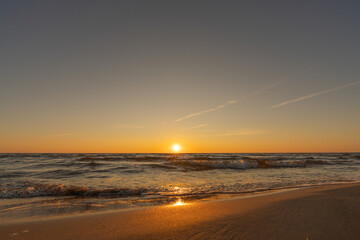 Obraz premium Sunset in a cloudless sky on the coast of the Gulf of Finland in Ust-Narva. The sky is clear, the waves gently roll on the sand. Estonia, Narva-Jyesuu. Natural background. Space for text.