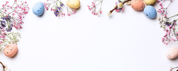 Beautiful Easter banner with spring flowers and colorful quail eggs over white background. Springtime and Easter holiday concept with copy space. Top view