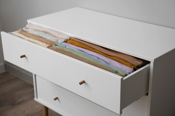 Open drawer with folded clothes in room, closeup