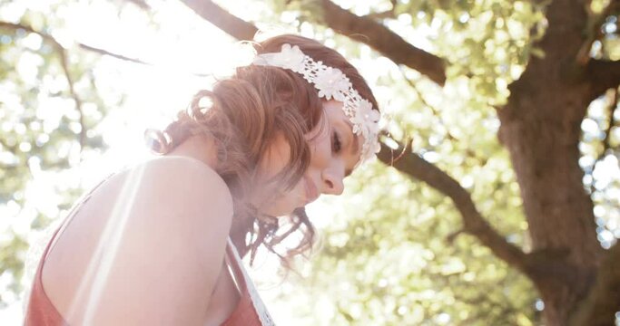 Closeup of a girl in a boho fashion vintage lace headband smiling quietly in a summer park with gentle sun flare
