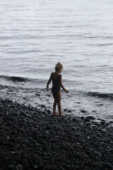 Adorable little girl on the huge empty black pebbled beach