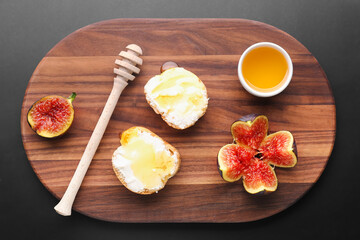Wooden board of tasty sandwiches with cream cheese, honey and fresh fig on dark background