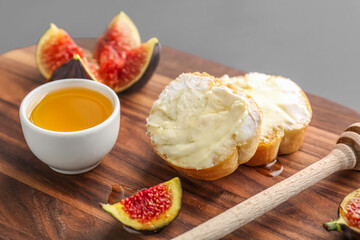 Wooden board of tasty sandwiches with cream cheese, honey and fresh fig on dark background, closeup