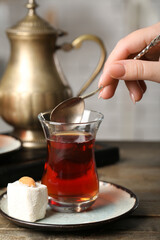Woman stirring Turkish tea on wooden table, closeup