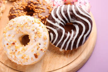 Wooden board with delicious donuts on lilac background, closeup