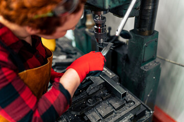 A young woman in STEM measures the diameter of a drill bit before starting work on a new project, uses protective equipment and practices safe work