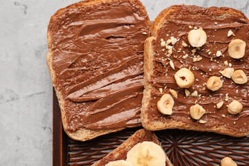 Wooden board of tasty toasts with hazelnut butter and nuts on light background, closeup