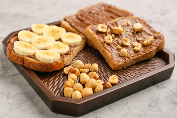 Wooden board of tasty toasts with hazelnut butter, banana and nuts on light background, closeup