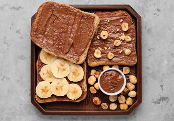 Wooden board of tasty toasts with hazelnut butter, banana and nuts on light background