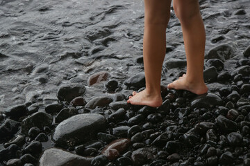 Child's feet barefoot on pebble beach near sea. Walking barefoot strengthens the muscles in...