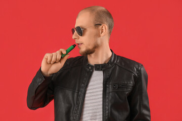Young man in sunglasses with disposable electronic cigarette on red background