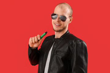 Young man in sunglasses with disposable electronic cigarette on red background