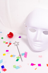 Artistic carnaval or costume party still life concept with white mask, clown nose, magic wand and confetti on white background