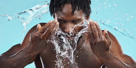 Water, splash and cleaning face for hygiene with a model black man in studio on a blue background...