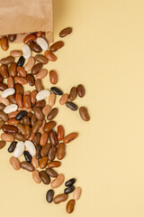 Brown bean mix spilling out of the kraft paper bag on a beige or yellow background top view