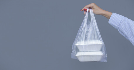Woman's hands holding PVC plastic bag with takeaway foam lunch boxes. Single use food containers, donation concept.