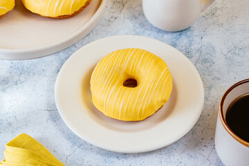 lemon doughnut in yellow glaze, coffee in a glass.