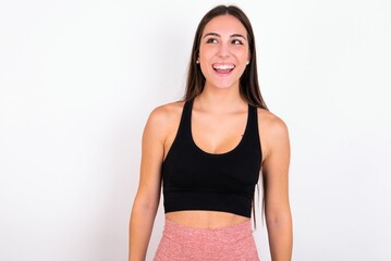 Surprised young woman wearing sportswear over white studio background, shrugs shoulders, looking sideways, being happy and excited. Sudden reactions concept.