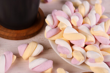 Plate with delicious twisted marshmallows and cup on light wooden table