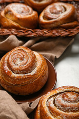 Plate and wicker basket with delicious cinnamon rolls on white table