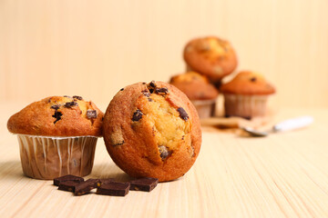 Delicious muffins with chocolate on beige wooden background