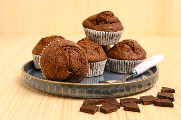 Plate with delicious chocolate muffins on beige wooden background