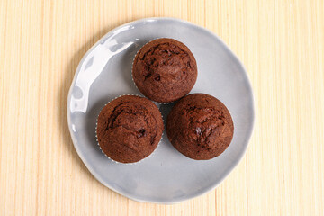 Plate with delicious chocolate muffins on beige wooden background