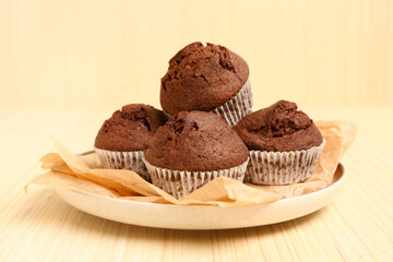 Plate with delicious chocolate muffins on beige wooden background