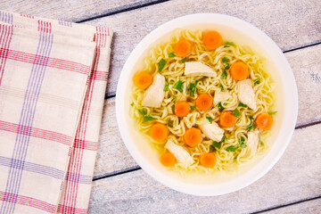 Chicken noodle soup with parsley and vegetables in a white plate,on a gray wooden background.