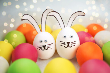 Funny bunnies couple on background of colorful eggs and bokeh. Cheerful Easter party background. Holiday card