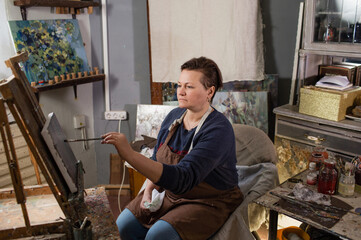 a professional female artist is engaged in painting on canvas in the studio. The artist paints a picture in her studio