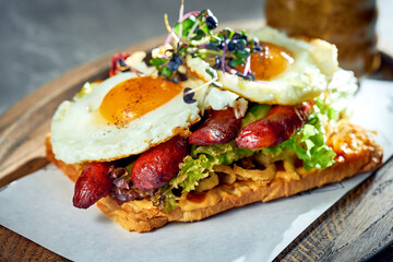 Toast with scrambled eggs with yolk, sausages on a board. Concrete background, morning light. Eggs for breakfast. Close up