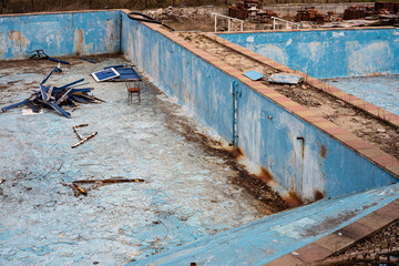 Abandoned pool with debris and a chair on the bottom. - 569127878