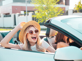 Portrait of two young beautiful and smiling hipster female in convertible car. carefree women...