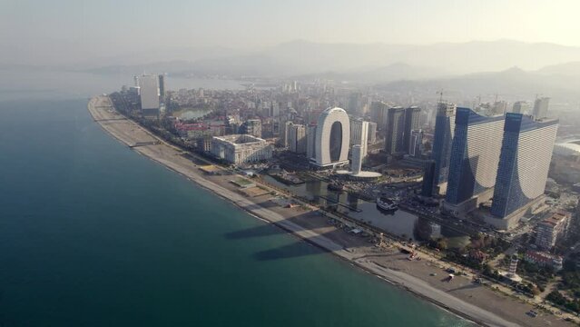 Aerial view of the coast of Batumi. Tall buildings on the embankment. The city of the Black Sea. Mountains hide behind the city.