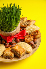 Plate with treats and grass on yellow background, closeup. Novruz Bayram celebration
