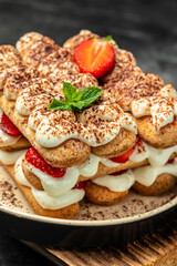 Italian dessert tiramisu cake with fresh strawberry, biscuit and whipped cream and mint on a dark background, Vegan lactose free dessert