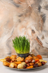 Plate with treats and grass on table near grunge wall. Novruz Bayram celebration
