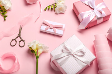Fototapeta na wymiar Composition with gift boxes, wrapping paper and freesia flowers on pink background. Women's Day celebration