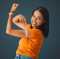 Vaccine, plaster and portrait of a woman in a studio with a strength gesture after being vaccinated. Happy, smile and proud female model with a vaccination band aid isolated by a dark blue background - obrazy, fototapety, plakaty
