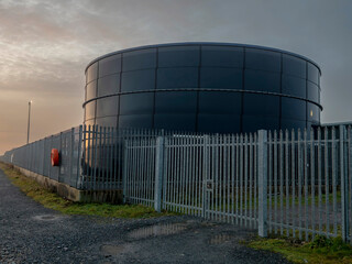 Tank for diesel or petrol fuel storage behind metal security fence at sunset. Oil industry supply...