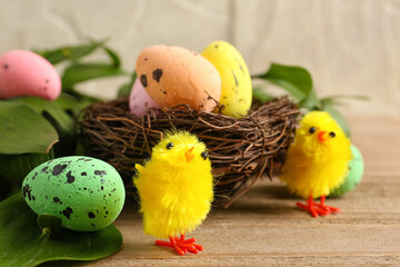 Nest with Easter eggs, toy chicks and plant leaves on wooden table, closeup