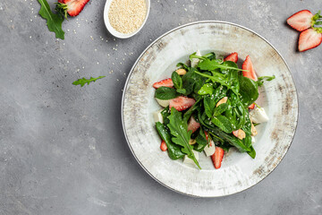 Fresh vegetarian salad with strawberry, spinach leaves and feta cheese on gray stone background, banner, menu, recipe place for text, top view