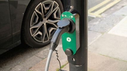 Electric vehicle charging at a public charging station in a city setting. New energy vehicles, eco-friendly alternative energy for cars. Electric cars are becoming more common and gaining popularity.
